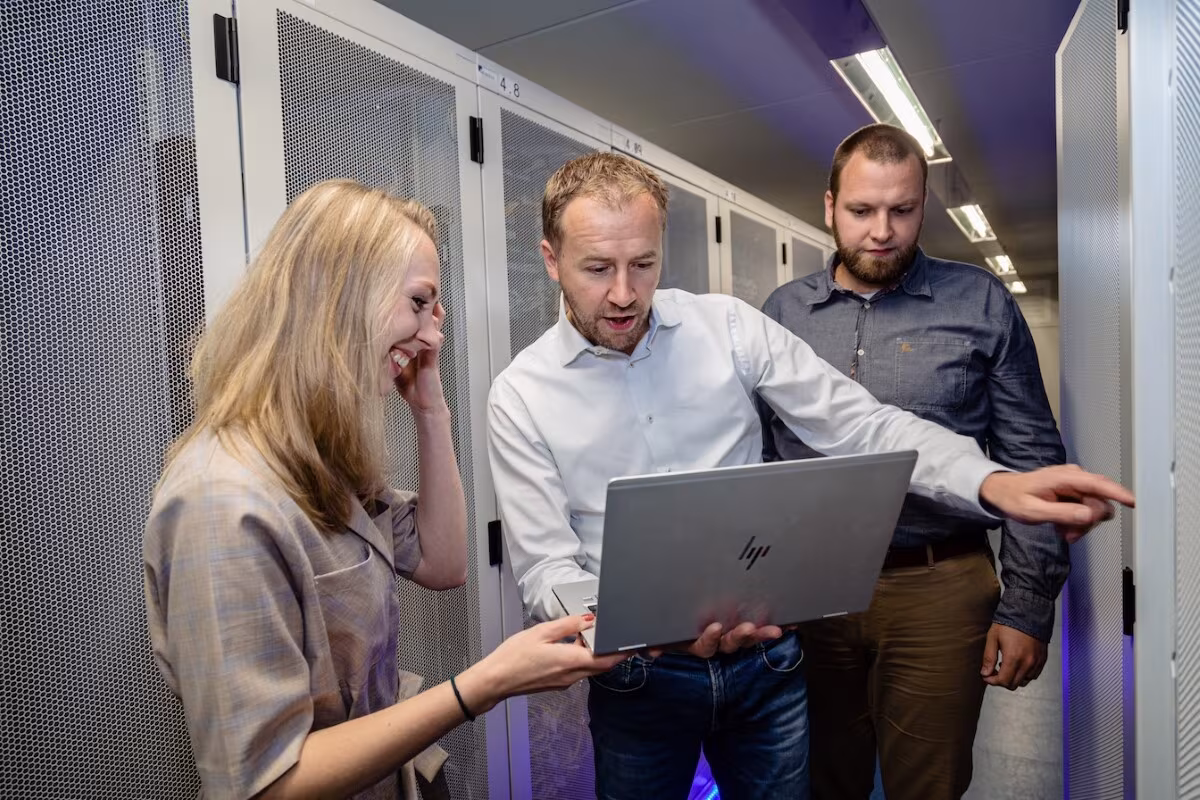 Drie collega’s van Techni Team kijken samen naar een laptop in een datacenter