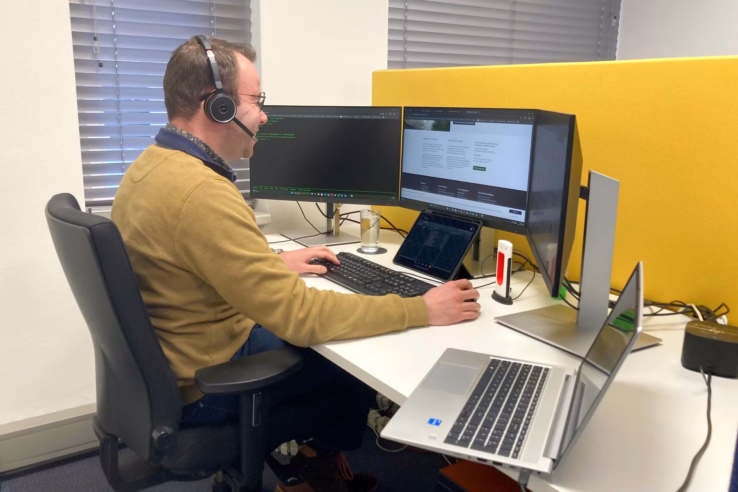 Collega van Techni Team met headset werkt aan een bureau met twee beeldschermen