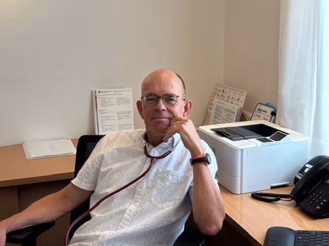 Arjen de Jager, huisarts, zit aan zijn bureau met een stethoscoop om zijn nek