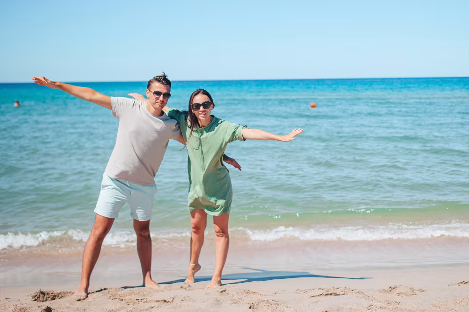 Stel staat met uitgestrekte armen op een strand aan zee