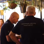 Twee collega’s van Techni Team in zwarte poloshirts, gezien van achteren, tijdens een bijeenkomst