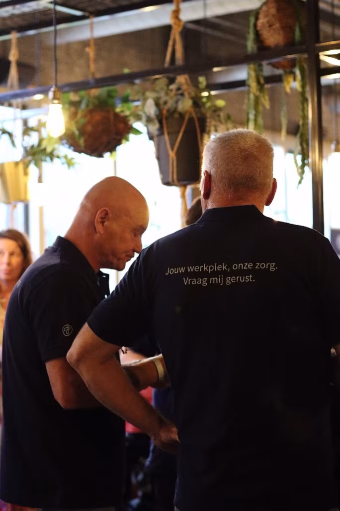 Twee collega’s van Techni Team in zwarte poloshirts, gezien van achteren, tijdens een bijeenkomst