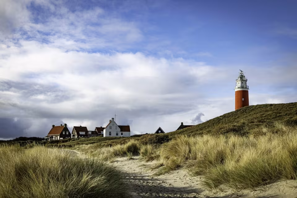 Rode vuurtoren van Texel tussen duinen en huisjes onder een bewolkte lucht