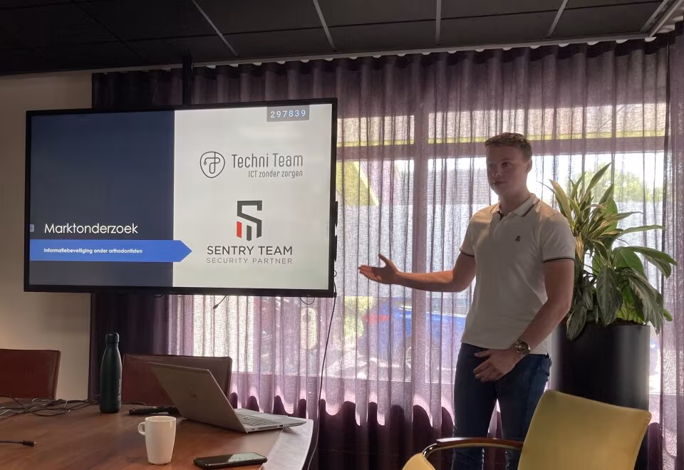 Stagiair geeft een presentatie over marktonderzoek bij Techni Team, naast een beeldscherm met slides