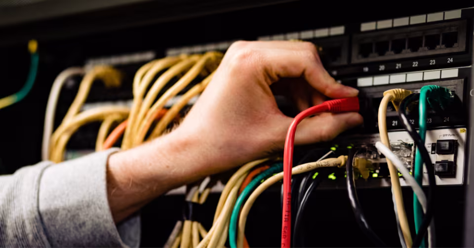 Hand steekt een rode kabel in een patchpaneel vol netwerkkabels