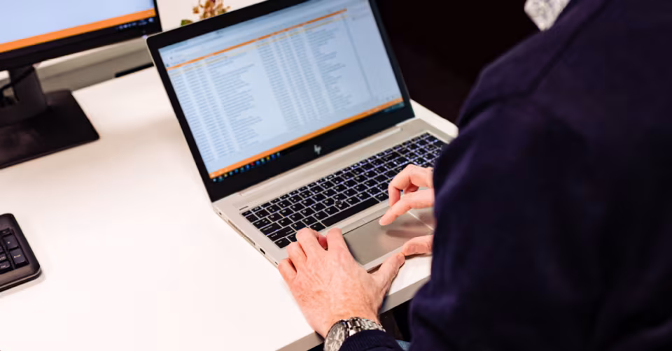 Persoon werkt op een laptop met een lijst op het scherm, gezien over de schouder