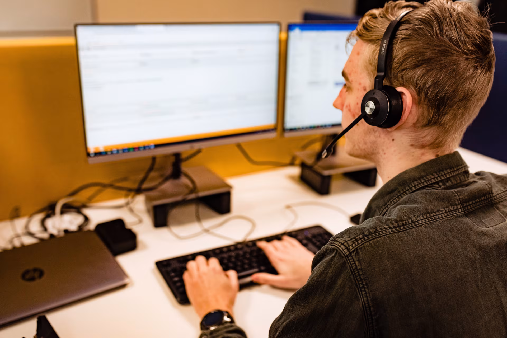 Collega van Techni Team met headset typt achter twee beeldschermen